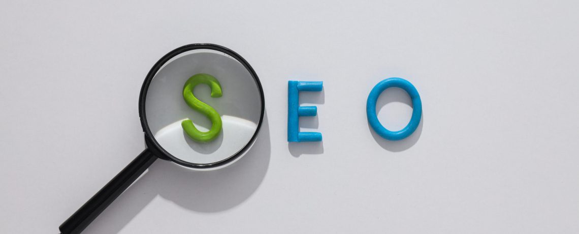 Letters SEO and magnifying glass on light background, top view