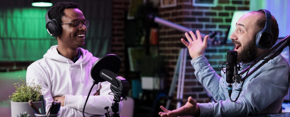 POV of male bloggers vlogging podcast talk on camera, using streaming equipment in studio with neon lights. Content creators having fun filming online episode for social media.